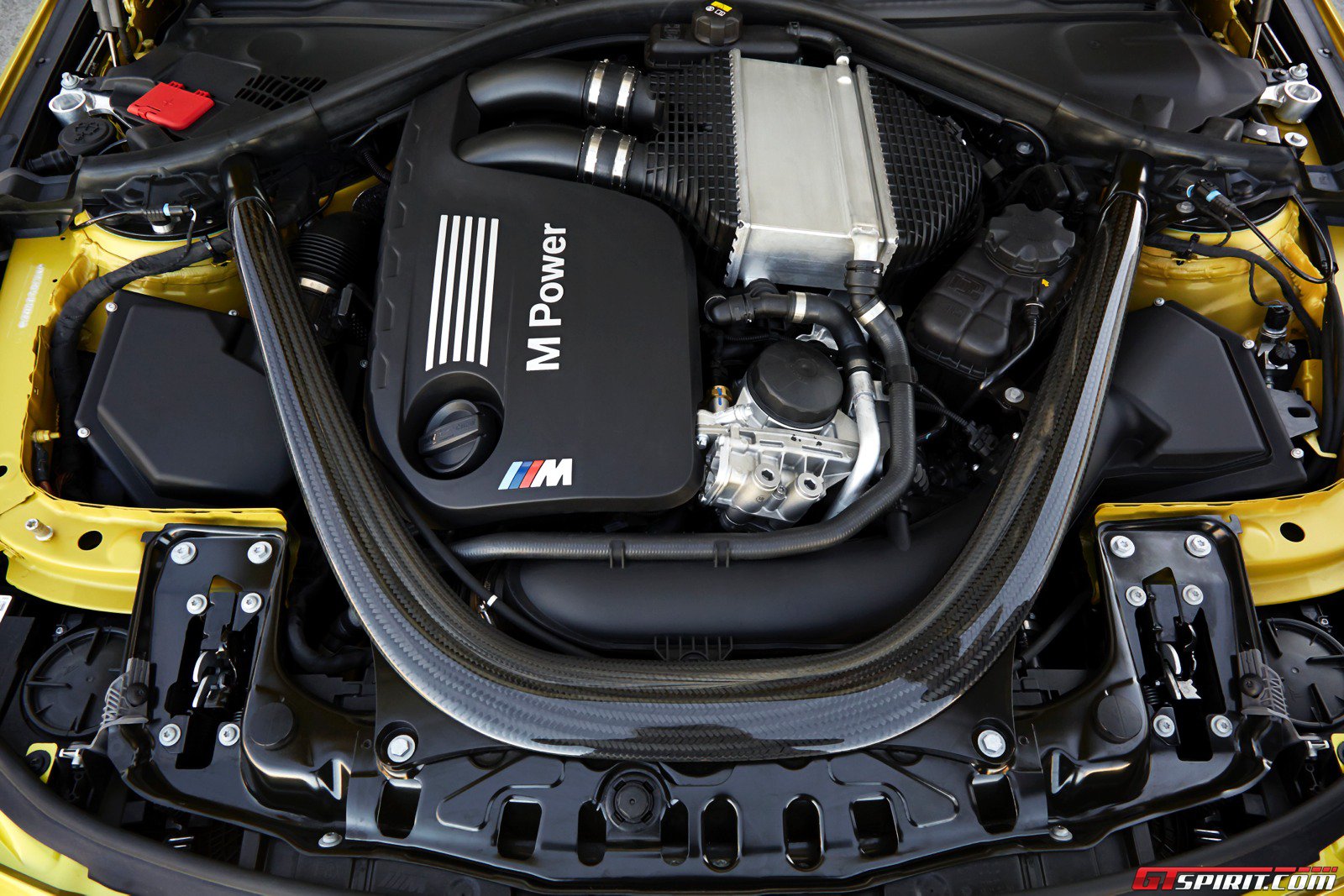 Engine bay photo of a BMW M4 F82 showing the S55 turbo inline-six layout and BMW M engine cover